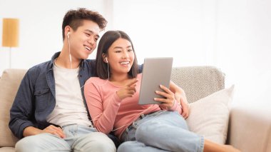 Neşeli Asyalı çift, dijital tablet kullanarak hafta sonları evlerinde kanepede oturup birlikte internete bakıyorlar. Koreli Aile Bilgisayar, Gadget ve Uygulamalarla Çevrimiçi Filmden Hoşlanıyor.