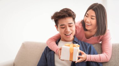 Romantik bir hediye. Çinli kız arkadaş sürpriz bir şekilde sevgilisine paketlenmiş bir kutu veriyor evde koltukta birlikte oturarak tatilini kutluyor. Tatil kutlamaları, doğum günleri ve Noel hediyeleri ve hediyeler