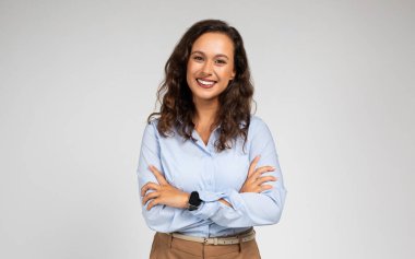 Güler yüzlü, kendine güvenen bin yıllık beyaz bayan yönetici göğsünde çapraz kollar olan resmi giysili öğretmen, arka planda gri bir arka plan stüdyosu var. Çalışma, öğrenim, kurslar ve iş