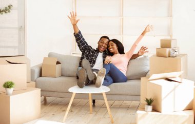 Karton kutuların arasında koltukta oturan mutlu siyah çift yeni eve taşındıkları için heyecanlılar. Genç Afro-Amerikan aile dairelerinde eşyalarını boşaltmaya ara verdi.