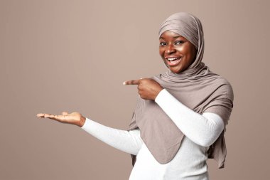 Şuna bak. Boş avucundaki bir şeyi işaret eden tesettürlü siyahi, tesettürlü, tesettürlü, başörtülü Afrikalı Müslüman kadın tasarımınız için bedava fotokopi yeri gösteriyor.