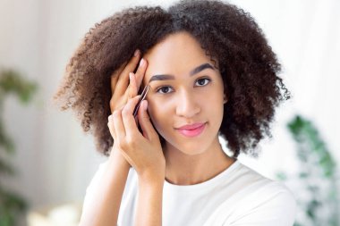 Evde güzellik tedavileri, prosedürler ve kaş şekillendirme. Sakin bin yıllık çekici Afrikalı Amerikalı kadın oturma odasının iç kısmında kaş kılı yoluyor, panorama, boş yer.