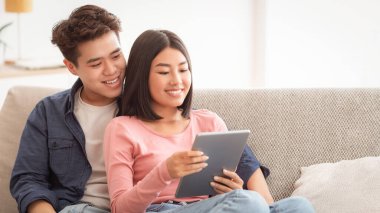 Neşeli Asyalı çift dijital tablet kullanıyor. Evdeki koltukta birlikte oturuyorlar. Koreli Kız Arkadaş ve Erkek Arkadaş İnternette Gadget Film Kullanıyor, Hafta sonu İzleme Konsepti