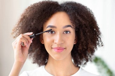 Gündüz vakti, doğal makyaj, güzellik ve modern kozmetik ürünleri. Çekici genç Afro-Amerikalı kadın kirpiklerine rimel sürüyor oturma odasının içinde fırçayla, kapat, boşluğu kopyala