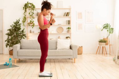 Başarılı diyet yaptıktan ve kilo verdikten sonra evde kilo verdikten sonra kendini tartan neşeli, sıska siyah kadın. Zayıflama, vücut bakımı. Metin için Boş Boşluk