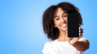 Pozitif ifade. Binlerce yıllık neşeli Afro-Amerikan kadın pembe tişörtlü, kıvırcık saçlı, menekşe arka planında boş ekranlı akıllı telefona odaklan, boş alan, stüdyo çekimi.