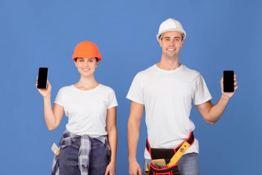 Siyah ekranlı akıllı telefonları tutan, web sitesi veya uygulama tasarımı için boş fotokopi alanı gösteren, mavi stüdyo arkaplanının başında duran,