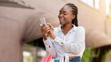 Düzenli müşteriler için özel bir teklif. Gülen Afro-Amerikalı kız renkli alışveriş torbalarıyla telefonla mesaj aldı, kapat, kopyala...