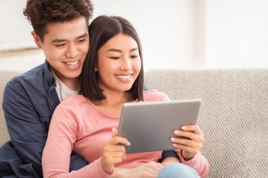 Mutlu Japon Çifti Evde Oturarak Dijital Tablet İzliyor. Kız arkadaş ve erkek arkadaş bilgisayar kullanarak rahatlıyor, hafta sonunu birlikte geçiriyorlar. Gadgets ve Modern Yaşam Tarzı.