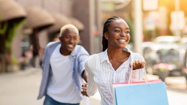 Vay canına, benimle butiğe gel. Çok renkli çantaları olan mutlu Afro-Amerikalı kadın erkekleri alışverişe, güneş ışığına götürdü.