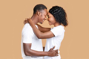 Siyah aşıklar sarılıp birbirlerine bakıyorlar, alınlarıyla dokunuyorlar, sarı stüdyo arka planı, fotokopi alanı. Duygusal Afrikalı Amerikalı erkek ve kadın kucaklaşıyorlar, romantik bir an yaşıyorlar.