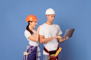 Ev onarımı sırasında dizüstü bilgisayar kullanan genç bir çift mavi arkaplan üzerinde bilgisayar başında duruyor, çevrimiçi onarım araçlarını arıyor, internetteki alışveriş inşaat malzemeleri, ücretsiz alan