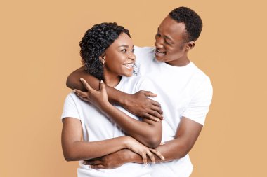 Sarı stüdyo arka planında poz veren neşeli Afrikalı Amerikalı genç çift, fotokopi alanı. Mutlu siyah erkek ve kadın kucaklaşıyorlar ve birbirlerine bakıyorlar, aşklarının her anının tadını çıkarıyorlar.