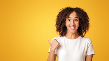 Güzel teklif. Heyecanlı, gülümseyen Afro-Amerikalı bir bayan, büyük satışlardan memnun, iyi fiyatlar, reklam için kopya alanı gösteriyor, sarı arka planda, stüdyo çekimlerinde, panoramada izole edilmiş.
