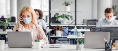 COVID-19 salgını sırasında müşteriyle uzaktan çalışmak. Bin yıllık koruyucu maskeli kadın akıllı telefonda konuşuyor ve modern ofis içi bilgisayarında daktilo yazıyor, boşluğu kopyala