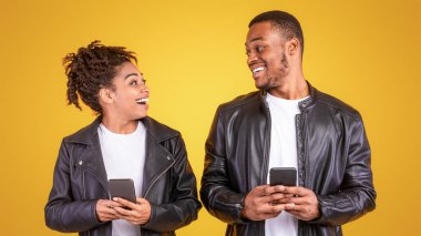 Çevrimiçi Sohbet İçin Akıllı Telefon Mesajı Kullanan Afro-Amerikan Çift Sarı Stüdyo Arkaplanının Üzerinde Duruyor. Mobil İletişim ve Telefon Uygulamaları Kavramı