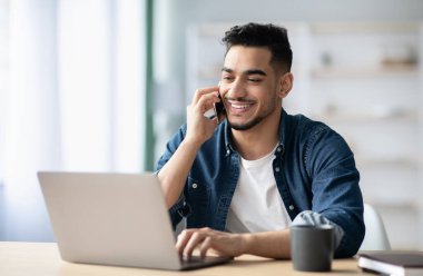 Başarılı bir ortadoğulu adam, evde çalışırken ortaklarıyla cep telefonuyla konuşuyor, akıllı telefon tutuyor ve dizüstü bilgisayara bakıyor, Arap serbest çalışanı iş görüşmesi yapıyor, uzayı kopyalıyor.