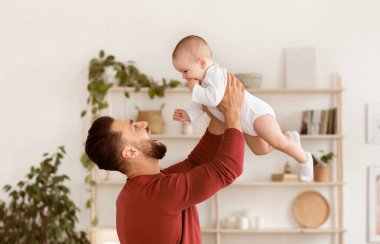 Mutlu baba, bebek yürüten çocukla oynuyor. Başının üstünde sarılıyor ve evde birbirimize bağlanıyoruz. Babaların Sevgisi, Babalığın Neşesi ve Ebeveynlik Konsepti.