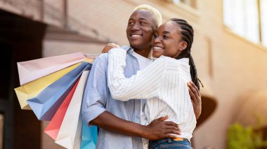 Birlikte eğlenin ve alışveriş yapın. Gülümseyen Afro-Amerikan çifti alışveriş merkezinde kağıt poşetlerle, güneş ışığıyla, boş alanla
