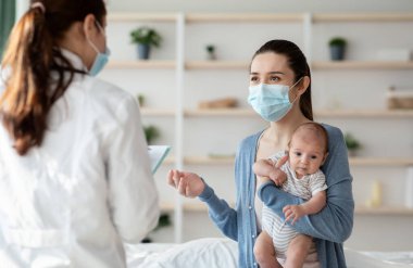 Koruyucu tıbbi maskeli tanınmayan bir doktor yeni doğmuş bebeğiyle annesini evinde ziyaret ediyor, bin yıllık anne ve bebeği koronavirüs salgını sırasında tedavi görüyorlar, seçici bir şekilde odaklanıyorlar.