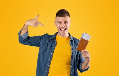 Heyecanlı milenyum adamı mavi arka plan üzerinde pasaport ve uçak biletlerini işaret ediyor.