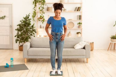 Kilo Verme Motivasyonu. Gülümseyen Afrikalı Kadın, zayıflamayı ve kilo vermeyi başardıktan sonra evde poz vermeyi tartıyor. Metin için Tam Uzunluk, Boş Alan