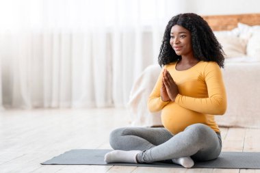 Huzurlu siyahi hamile kadın evde meditasyon yapıyor, fotokopi odasına bakıyor, yatak odasına bakıyor. Mutlu Afro-Amerikan beklenen kadın sabah yogası yapıyor, nilüfer minderinde oturuyor.