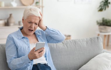 Mobil Dolandırıcılık Konsepti. Smartphone Screen 'e bakan yaşlı bir kadın hayal kırıklığıyla kafa kafaya verip evde boş bir yerde, koltukta oturuyor.