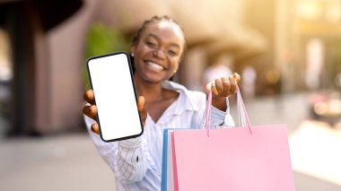Mobil uygulama ile mağazalarda büyük indirimler. Siyah alışveriş torbalı Afrikalı Amerikalı kız mutluluğunu ifade ediyor ve boş ekranlı akıllı telefon gösteriyor.