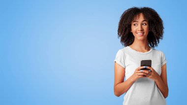 Yazışmalar, sohbet, modern cihazlar, sosyal medya reklamı ve iyi bir mesaj. Gülümseyen bin yıllık Afro-Amerikan bayan akıllı telefonu tut ve boş alana bak, mor arka planda izole edilmiş, stüdyo çekimi