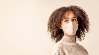 Grip, grip ve virüs, solunum hastalıkları, karantina ve salgın hastalık. Modern koruyucu maskeli ve süveterli Afrikalı Amerikalı genç bir kadın ışık arka planında izole edilmiş boş alana bakıyor.