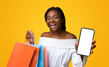 Kolay ödemeler. Alışveriş torbaları ve kredi kartı pozu ile neşeli genç siyah kadın sarı stüdyo arka planında, neşeli Afrikalı kadın mevsimlik alışverişin ve nakit para kazanmanın keyfini çıkarıyor, kopyalama alanı