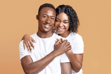 Portrait of loving african american young couple posing on studio background yellow. Beautiful black man and woman hugging and smiling at camera, happy to be together, relationships concept