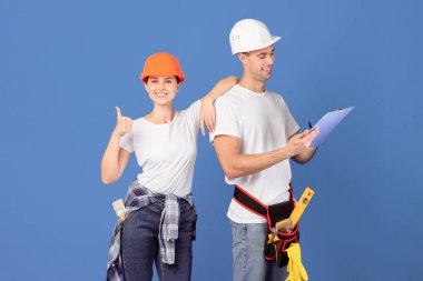 Profesyonel Tamir Servisi. Hardhat 'lı İşçi Çifti Yenileme Planıyla Bekletmekten ve Başparmağımı Yukarı Göstermekten Mavi Arkaplanda Birlikte Durmaktan, Boşluğu Kopyalamaktan Mutlu Ol