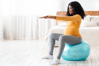 Siyahi kadın baloda antrenman bekliyor, doğum için hazırlanıyor. Koca göbekli, gülümseyen Afrikalı hamile kadın yatak odasında spor salonunda oturup fotokopi odasına bakıyor. Hamilelik sırasında spor