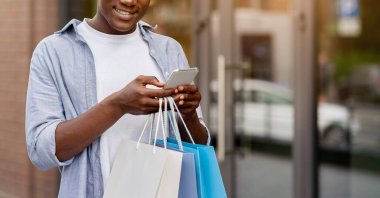 Mağaza hakkında iyi eleştiriler. Beyaz saçlı, gülümseyen Afro-Amerikan adam, alışveriş merkezinin yakınından alışveriş yaptıktan sonra renkli çantalı.