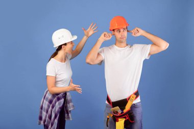 Tadilat sırasında tartışan kasklı bir çift, makine dairesinde anlaşmazlık yaşayan, parmaklarıyla kulaklarını tıkayan bir adam, duygusal bir kadın mavi arka planda ona bağırırken,