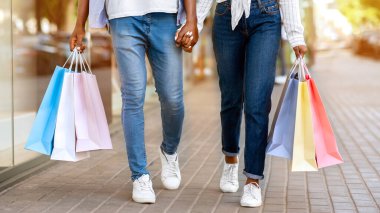 Yaşam tarzı alışverişi. Sokakta kesekağıdıyla dolaşan kot pantolonlu Afro-Amerikan genç adam ve kadın.