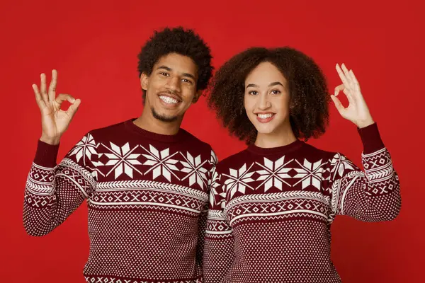 Harika bir yeni yıl ve Noel partisi. Benzer kazaklar giyen neşeli Afro-Amerikan aileleri işaret levhasını elleriyle gösteriyorlar ve kameraya bakıyorlar, kırmızı arka planda izole edilmiş, boş alan, stüdyo çekimi.