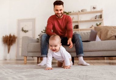Mutlu baba, evdeki oturma odasında yerde sürünen bebeğe bakıyor. Babamın küçük bebeğe bakması için babalığı bırakması. Çocuk bakımı, şirin babalık anları. Seçici Odaklanma