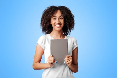 Pozitif ifade ve online galibiyet. Pembe tişörtlü, kıvırcık saçlı, mutlu ve elinde dijital tablet bulunan, mor arka planda, boş alanda, stüdyo çekimlerinde izole edilmiş Afro-Amerikan kadını.