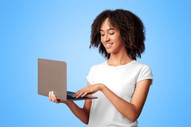 Covid-19 tecridi sırasında uzaktan çalışma, eğitim ya da blog yazma ve arkadaşlarla sohbet. Gülümseyen bin yıllık Afro-Amerikan kadın dizüstü bilgisayarda yazıyor, mor arka planda izole edilmiş, boş alan, stüdyo çekimi