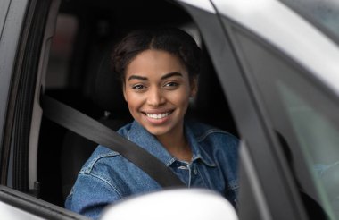 Büyük otomobil teklifi, araba reklamı ve modern blog yazarı. Gülümseyen mutlu Afro-Amerikan kadın direksiyonun arkasında oturuyor emniyet kemeriyle ve boş bir pencereden dışarı bakıyor.