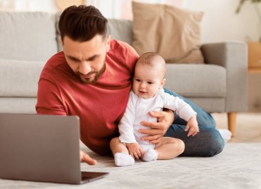 Küçük oğlu olan baba dizüstü bilgisayar kullanıyor, internete bakıyor ve birlikte film seyrediyor evde yerde oturup dinleniyor. Babalık, Babalık İzni Konsepti. Seçici Odaklanma