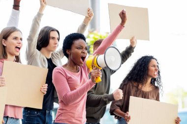 Çok ırklı genç göstericiler ellerinde megafon ve boş pankartlarla sokağa saldırıyorlar. Açık havada protesto eden, insan haklarını savunan boş pankartlı uluslararası bir grup insan.