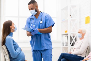 Coronavirus salgını sırasında doktor randevusu. Erkek hemşire, hastanede hamile bir kadınla konuşuyordu. Tıbbi Tedavi, Covid-19 Salgın Konsepti. Seçici Odaklanma