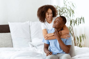 Boş zamanlarında rahat bir yatakta eğlenmek. Mutlu çift rahat bir evde birlikte gülüyor, neşeli bin yıllık Afro-Amerikan kadın sabahın köründe yatak odasının içinde adama sarılıyor, uzay fotokopisini çekiyor.