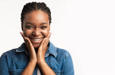 Ortodonti Konsepti. Beyaz arka plandaki kameraya gülümseyen, el pençe divan duran neşeli siyah kız. Stüdyo Çekimi