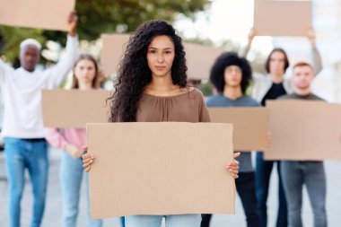 Sokaktaki bir grup göstericiye liderlik eden aktif, güzel bir genç kadın. İnsan ya da hayvan haklarını ve ırkçılığı protesto eden boş pankartlı uluslararası çeşitli insanlar.