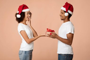 Yeni yıl için güzel bir hediye. Genç, yakışıklı, sakallı Afrikalı Amerikalı erkek kadınlara Noel hediyesi veriyor. Hoş bir sürpriz, arka planda izole edilmiş, boş bir yer, stüdyo çekimi, yan görüş.